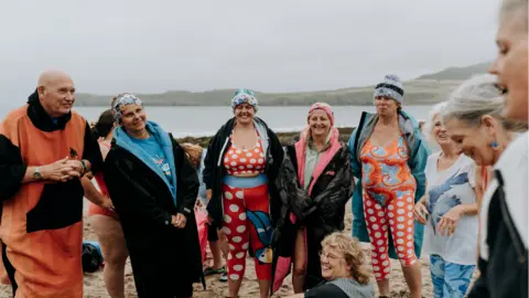 Ella Richardson A group of people stood on a beach in swimming wear laughing