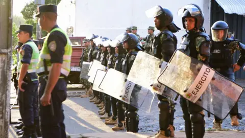 Policemen stand guard outside the Tacumbu prison to impede the entrance to the relatives of inmates, during an operation to regain control of the prison in Asuncion, on December 18, 2023. (