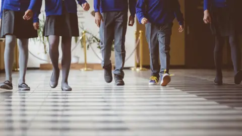 Getty Images Cropped image of school kids in uniform walking together in a row through corridor