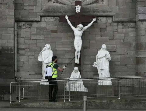 Brian Lawless / PA Media A man spraying disinfectant at a statue of the crucifixion of Jesus in Dublin on Good Friday