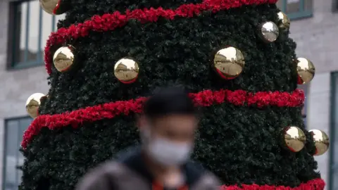 PA Media A masked man walks past a Christmas tree