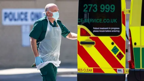 Getty Images London Ambulance staff wearing PPE help a patient with an unknown condition from an ambulance at Queens Hospital