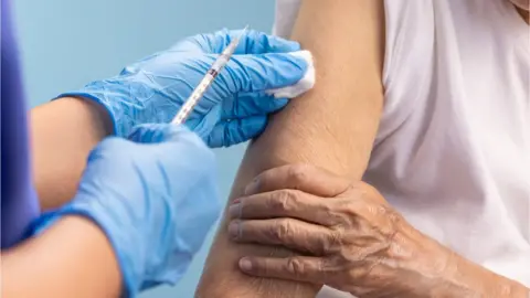 Getty Images/Toa55 Nurse vaccinating an older woman