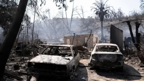 EPA Autos quemados yacen frente a la devastada casa de Patricia Araya, conocida como “La Pati”, empleada del Jardín Botánico de Viña del Mar, quien murió en un incendio junto a su madre y dos nietos, de 9 y 1 año. en Viña.  del Mar, Chile, 5 de febrero de 2024