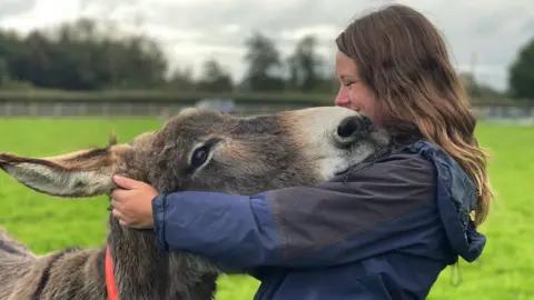 Victoria Gill/BBC Janneke Merkx with one of the donkeys at the Donkey Sanctuary
