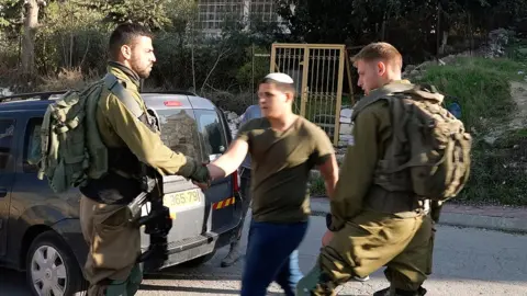 Gabrielle Weiniger An Israeli soldier (L) shakes hands with an Israeli settler (R) who attacked Yasser Abu Markhiya in Hebron, in the occupied West Bank