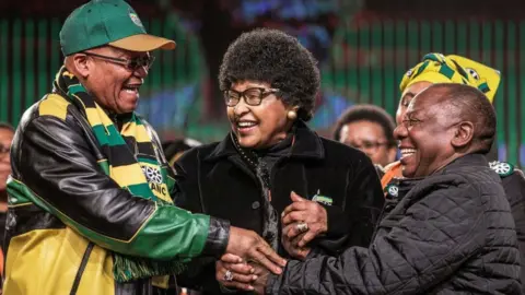 AFP Former wife of the late South African President Nelson Mandela, Winnie Mandela (C) holds the hands of South African President Jacob Zuma (L) and South African Deputy President Cyril Ramaphosa (R) during the opening session of the South African ruling party African National Congress policy conference on June 30, 2017 in Johannesburg.