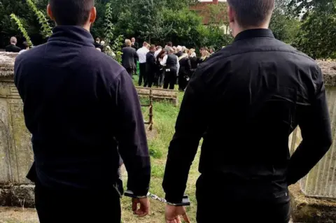 Lisa Selby / @bluebaglife Elliot Murawski in handcuffs at his grandfather's funeral