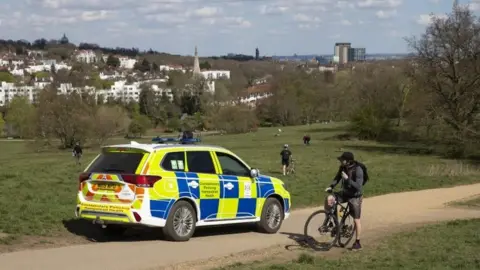 Getty Images A man is told by a police officer that there is no cycling at Parliament Hill Viewpoint in Hampstead Heath on April 04, 2020 in London, England.