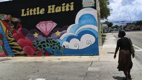 Getty Images Woman walking past mural of showing a sign of Little Haiti