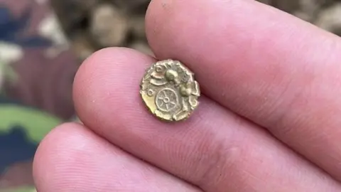 Jamie White A hand holding a tiny gold coin