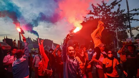 Getty Images Demonstrators light flares during a rally to mark International Labour Day in Surabaya, Indonesia.