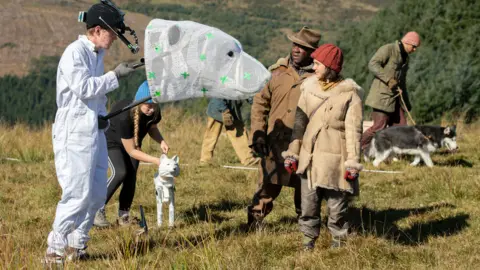 BBC | Bad Wolf | HBO Man holds a bear-like head in front of actress Dafne Keen