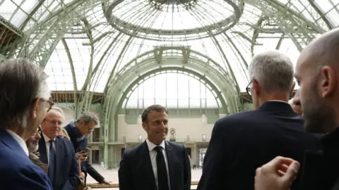 Getty Images France's President Emmanuel Macron (C) speaks during a visit in Le Grand Palais, in Paris, on April 15, 2024, 100 days ahead of the Paris 2024 Olympic Games.