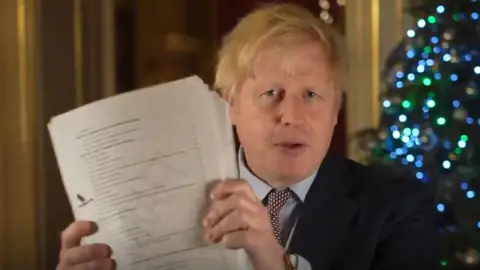 PA Media Boris Johnson holds up a draft of the Brexit deal document in video message on Christmas Eve 2020