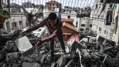Getty Images A man in Rafah clears rubble from a building hit by an airstrike