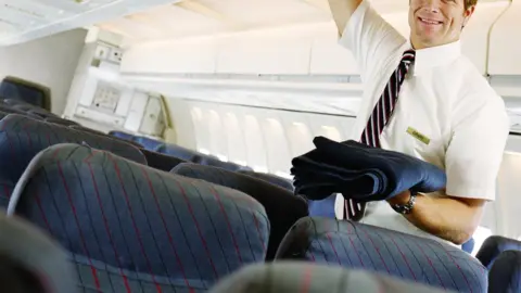 Getty Images A stock image of a male flight attendant putting a blanket in overhead locker