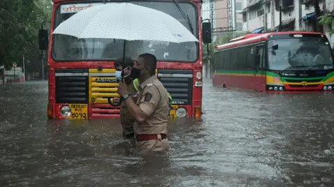 Getty Images A policeman helps a public transport driver to cross a flooded street due to heavy rain caused by cyclone 'Tauktae' in Mumbai.