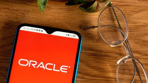 Getty Images The Oracle logo is seen on an Android smartphone, on a table next to spectacles and a plant in this staged product photo