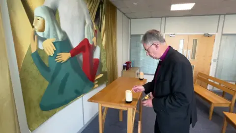 The Bishop of Oxford, the Reverend Steven Croft, bends to light a candle on an altar at Church House in Kidlington, which is the seat of the Diocese of Oxford. 