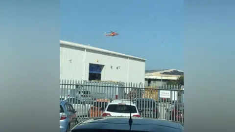 An air ambulance flying over grey buildings on an industrial estate.