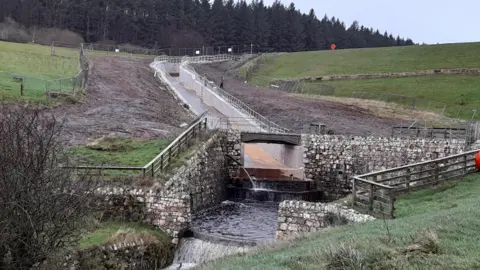 MANX UTILITIES The refurbished spillway at Cringle Reservoir, which is a long concrete channel with stone walls at the bottom directing the flow of water downhill.