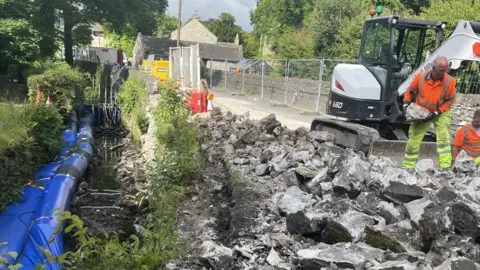 Collapsed retaining wall in Brough, Derbyshire with workers removing stones