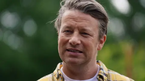 Jamie Oliver - head and shoulder image. He is wearing a yellow and grey checked shirt.