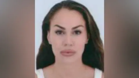 A woman with long brown hair is wearing a white vest