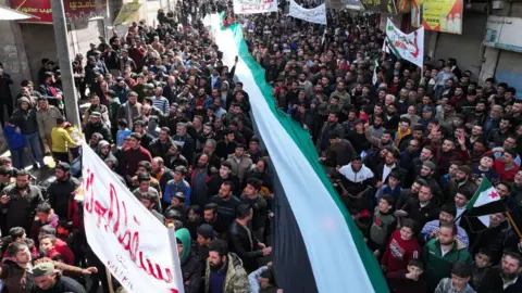 AFP People take part in a protest against Hayat Tahrir al-Sham (HTS) in the rebel-held town of Binnish, Idlib province, north-western Syria (8 March 2024)