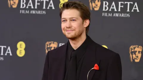 Getty Images Joe Alwyn with a single red flower on his dark suit