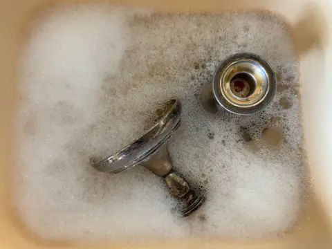 Richard Morasci Silver candlesticks in soapy water in a sink