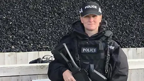 A female firearms officer in a police uniform wearing a cap and holding a gun