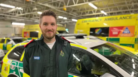 BBC Paramedic Jon Hall stands in front of ambulance vehicles