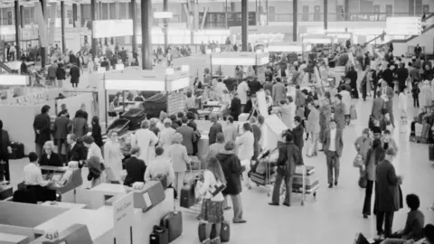 Getty Images Heathrow airport security terminals in 1975, a black and white photo shows people travelling through with bags