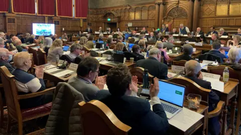 A meeting of the full council in Sheffield town hall chamber with many councillors sitting facing the Lord Mayor in an ornate wood panelled room