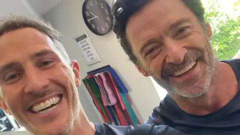 Jules Greenway A selfie taken by Jules Greenway, who is on the left, with Hugh Jackman on the right. Both are smiling.