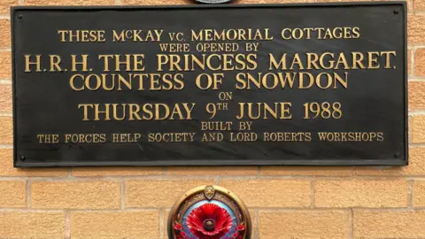 BBC/Simon Thake A plaque on the wall of a house with a poppy underneath