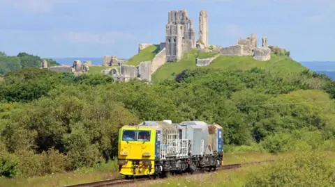 Andrew PM Wright A Multi Purpose Vehicle on rail tracks with the ruins of Corfe Castle in the background