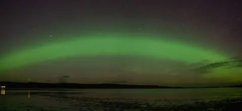 Gary Macleod The Northern Lights in the north coast of Scotland. There is a green arc in the sky with the sea and mountains below. 