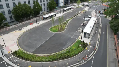 Swindon Borough Council A new oval-shaped bus station in Swindon seen from a drone shot with newly-planted shrubbery, red cones and new markings for bus stops. The area is fenced off.