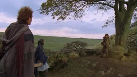 Warner Bros./Kevin Reynolds Kevin Costner, Morgan Freeman and Dan Newman in old costumes of cloaks and brown wool talk to each other beside the tree and wall