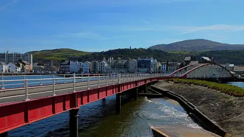 The swing bridge, which is a long red metal structure with white railings standing on black metal pillars over the inner harbour.