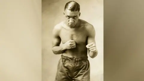 Michael Gains A black and white photo of a boxer raising his fist in a guard position