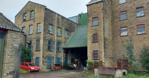 LDRS The back of the former Victor Works woollen mills on Bolton Hall Road in Bradford which could be turned into flats. A red car is parked close to part of the building which has a green sloping iron roof.