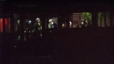 Night time shots showing rescue personnel inside a shopping centre, wearing protective equipment