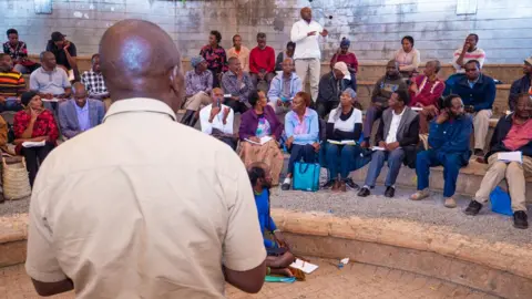 People listen to a man with his back to the camera