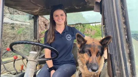 BBC Bethany Sharpe sitting in a tractor with her arm around her Alsatian dog, Willow 