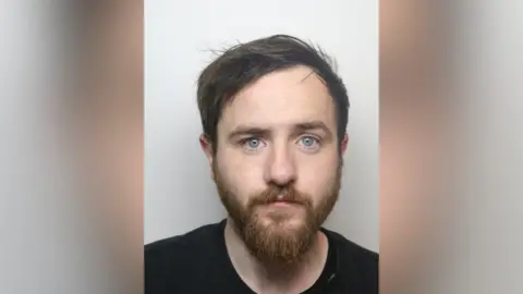 Police custody image of Shea Conley. He is a white man with dark hear and a beard.