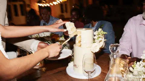 A wedding cake being cut with a wine glass next to it on the table.